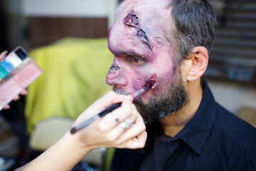 Zombie male makeup applying for halloween concept. Make up with brush and paint skin and blood face