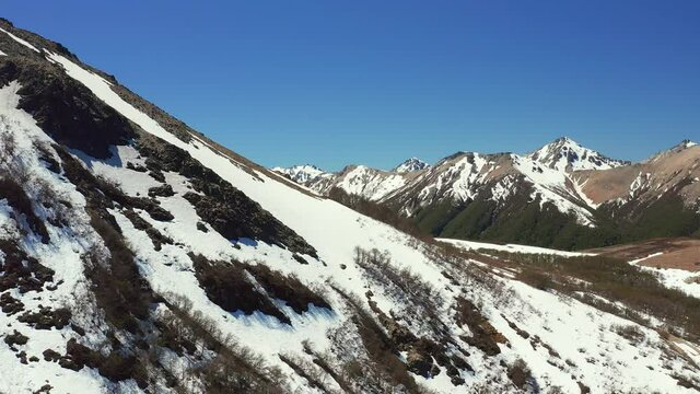Aerial drone dolly shot of mountain side in melt in spring at the Cerro Bayo ski resort near Villa La Angostura, revealing forest and rocks on the mountains