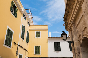 Fototapeta na wymiar Yellow and white houses facades with green closed wooden windows in Ciutadella Menorca