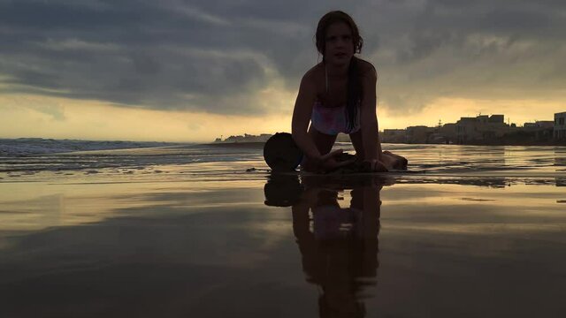 Unique low angle of beautiful caucasian little girl playing with bucket and sand on beach at sunset. Slow-motion