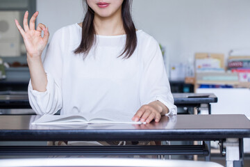 デスクで本を開いてサインを送る女性　
インを送る人