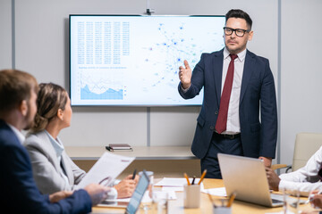 Serious business coach pointing at one of employees while answering his question during presentation