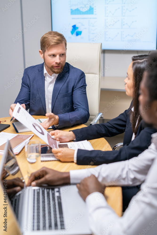 Poster confident businessman looking at one of two intercultural colleagues during discussion of working po