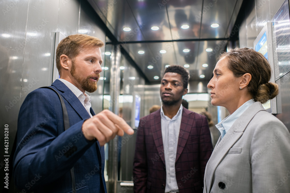 Aufkleber two of three young intercultural colleagues discussing something inside moving elevator