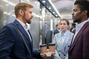 Group of multiracial colleagues in formalwear standing in elevator while moving to their office © pressmaster