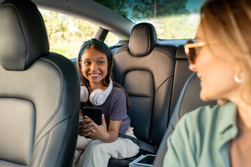 Happy daughter looking at her mom while sitting on backseat inside electric car