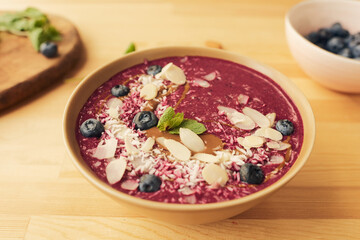 Bowl with fresh homemade smoothie decorated with blueberries, mint leaves, almond and coconut flakes