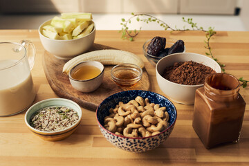 Group of bowls and jars with ingredients for smoothie on wooden kitchen table