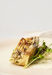 Plate with tasty baked cod fillet, greens and sauce on light background, closeup