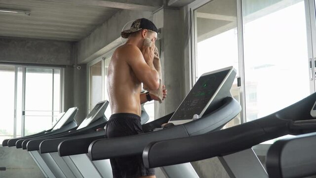 Handsome muscular man running on treadmill finished exercise drinking water and wiping sweat with towel in fitness gym . Shirtless sport guy workout  on running Machine. bodybuilder cardio training