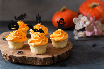 Festive Halloween cupcakes with scary toppings on vintage wooden board on dark background. Pumpkin cupcakes with black decorations. Bakery, confectionery menu