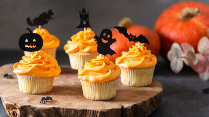 Cupcakes and pumpkin on a dark background. Sweets for the celebration of Halloween. Side view, horizontal. Bakery, confectionery menu