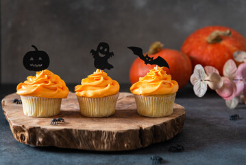 Festive Halloween cupcakes with scary toppings on vintage wooden board on dark background. Pumpkin cupcakes with black decorations. Bakery, confectionery menu. Side view