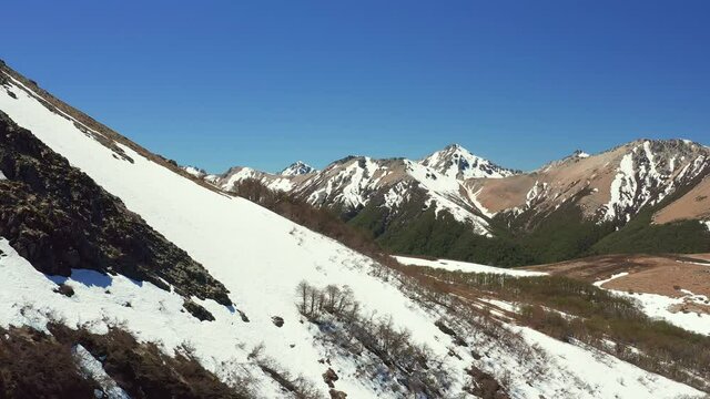 Aerial drone shot of ski slopes in melt in spring at the Cerro Bayo ski resort near Villa La Angostura, revealing forest and rocks on the mountains
