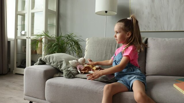 Excited child sitting on sofa playing with her stuffed toys while in living room at home.
