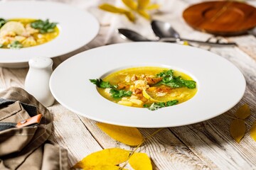 Delicious autumn soup with chanterelles and fresh herbs. Seasonal dish with edible mushrooms. White plate and cutlery on a rustic background. Food still life. Organic wild foods. Copy space