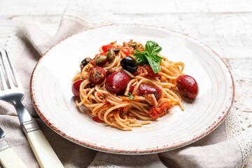 Plate of tasty Pasta Puttanesca on white wooden background