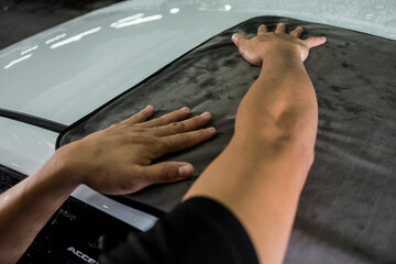 A man wiping dry the hood of a white SUV with a large microfiber towel.