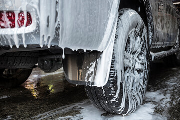 Foamy shampoo drips down from the rear bumper and mud flap of a SUV. During an exterior wash, part of car detailing service.