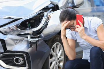 Upset woman talking on phone against background of broken car