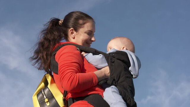 Woman with a baby in a sling ergo backpack traveling outdoor, family vacations adventure, mom with baby boy in infant kid carrier hiking. High quality 4k footage