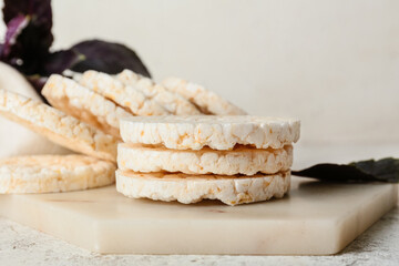 Board with puffed rice crackers on light background, closeup