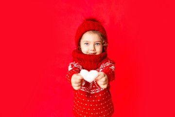 child a little girl in winter clothes holds a heart on a red background. New year's or Valentine's day concept, place for text