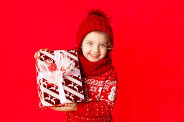 child a little girl in winter clothes holds a gift on a red background. New year's concept, space for text