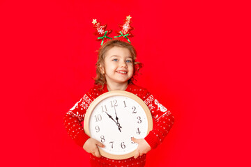 child a little girl in winter clothes holds a watch on a red background. New year's concept, space for text