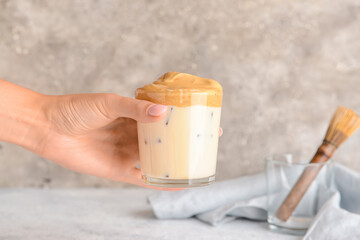 Woman holding glass of tasty dalgona hojicha latte at table