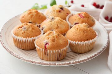 Plate with tasty cranberry muffins on light wooden background