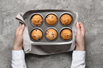 Woman holding baking tin with tasty cranberry muffins on grunge background
