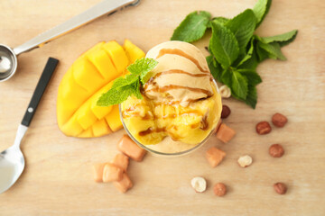 Bowl of delicious ice cream balls with caramels and mango on wooden background
