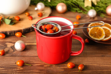 Cup of tasty rose hip tea and berries on wooden background