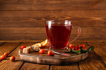 Glass cup of tasty rose hip tea and berries on wooden background