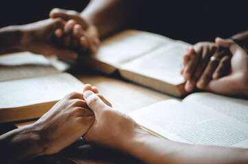 Christian group of people holding hands praying worship to believe and Bible on a wooden table for devotional or prayer meeting concept. - obrazy, fototapety, plakaty