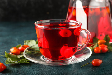 Glass cup of tasty rose hip tea and berries on black background