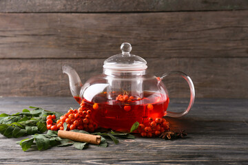 Glass teapot with tasty rowan tea on wooden background - obrazy, fototapety, plakaty