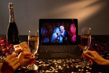 Birthday party. Online congrats. Video conference. Unrecognizable female friends with glass champagne getting congrats happy couple on tablet computer in holiday home interior.