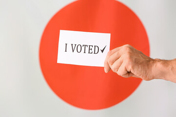 Hand holding paper with text I VOTED against flag of Japan