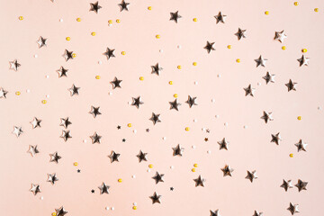 Festive beige solid color background with gold stars and sequins. Sequins and sparkling decorations top view.