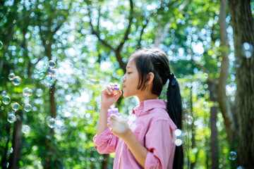 Fototapeta premium Adorable happy cute girl playful foam bubbles in green playground in summer outdoors. Funny Cheerful girl in the park with happy times.