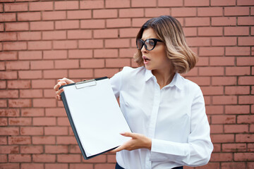 Business woman in white shirt and glasses with documents on the street brick wall