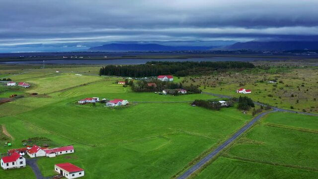 Panoramic View Of Green Meadow In Gardakirkjugardur Cemetery With Dirt Road, Some Houses And A Church At The Distant Near Reykjavik, Iceland. - Aerial Drone Shot