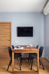 Stylish dining room interior with wooden table, black chairs and TV set.