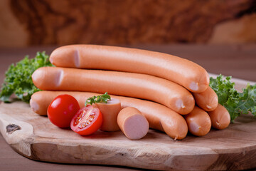 Styled Frankfurter sausages on wooden board with tomatoes and green herbs