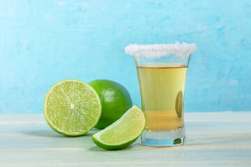 Tequila shot with lime slices, a Mexican drink on a vibrant blue background, with a salt rim, side view