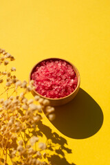 Wooden bowl filled with pink bath sea salt. Beauty treatment for spa and wellness with plant shadow. Skincare natural cosmetic concept for body care. Place for text