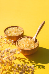 Wooden bowls with a spoon filled with yellow bath sea salt. Beauty treatment for spa and wellness with dry plants and shadows. Skincare natural cosmetic concept for body care