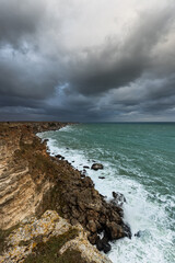 Sea wave crashing on rocky coast with dark clouds